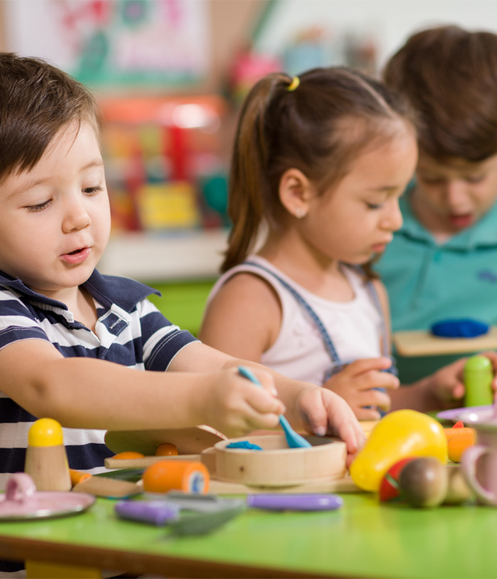 Three children engage in playful activity at a colorful table filled with various toys and craft materials, showcasing creativity and fun.